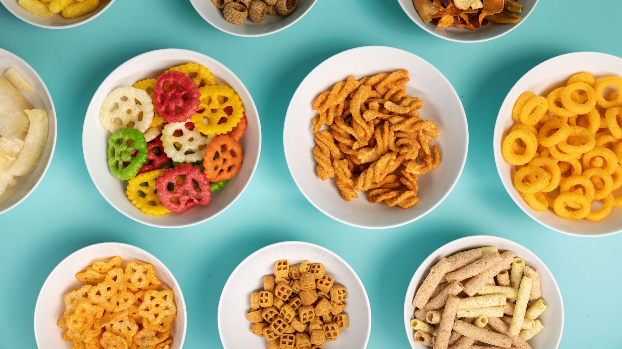 Multiple extruded snacks in bowls like finger chips, cheetoz, rings